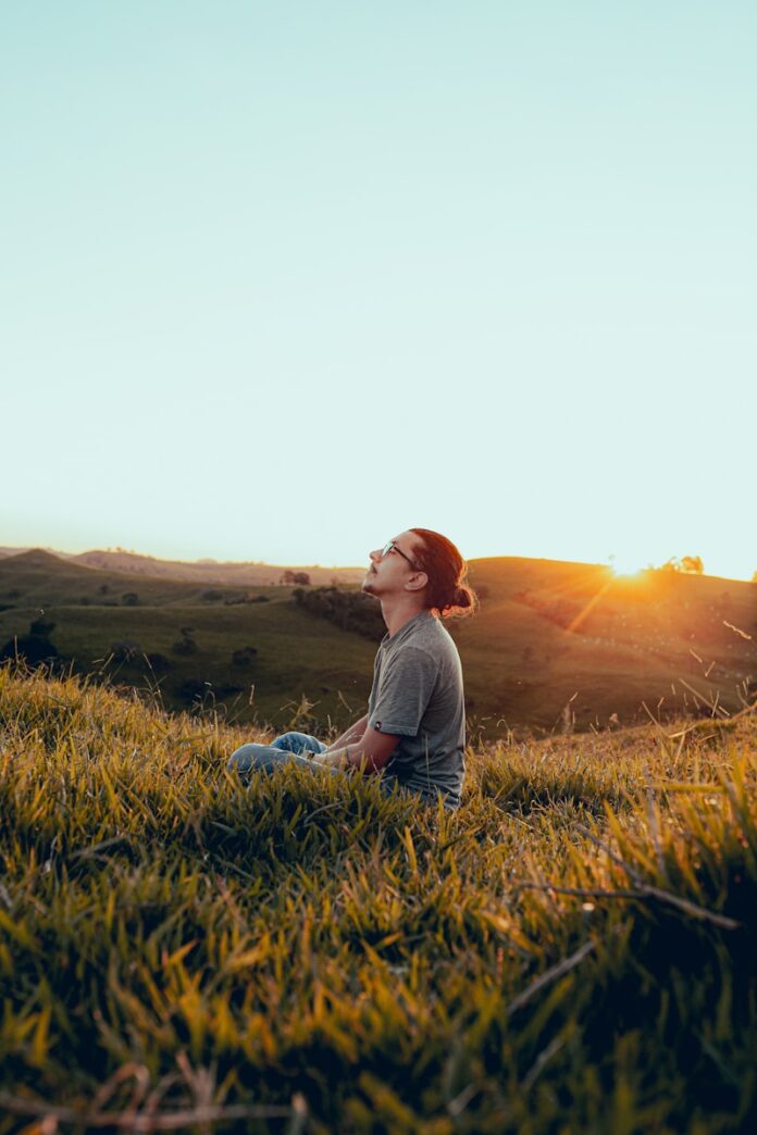 Photo by Guilherme Stecanella man in white shirt sitting on green grass field during sunset