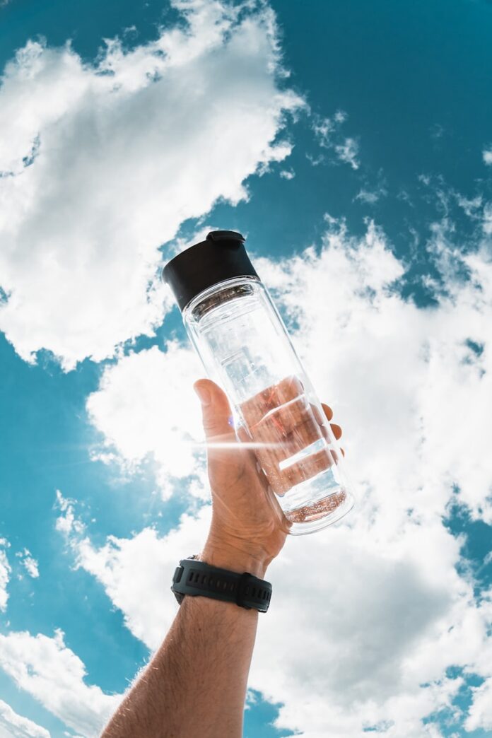 Photo by Jan Kopřiva a hand holding a water bottle in front of a blue sky