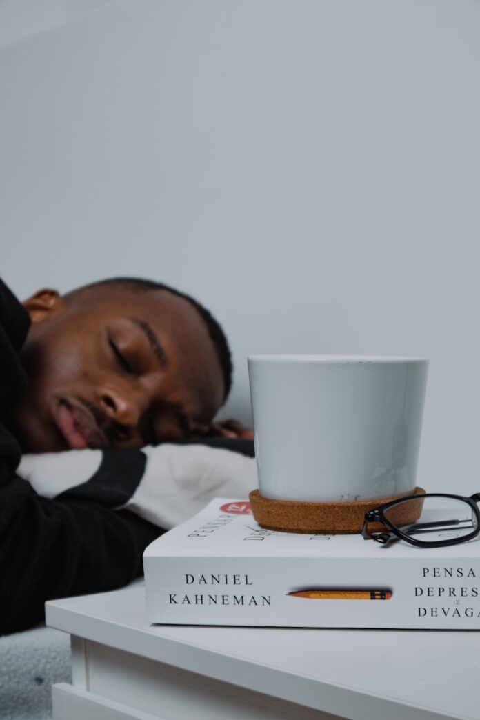 Photo by Nubelson Fernandes a man sleeping on top of a stack of books next to a cup of coffee